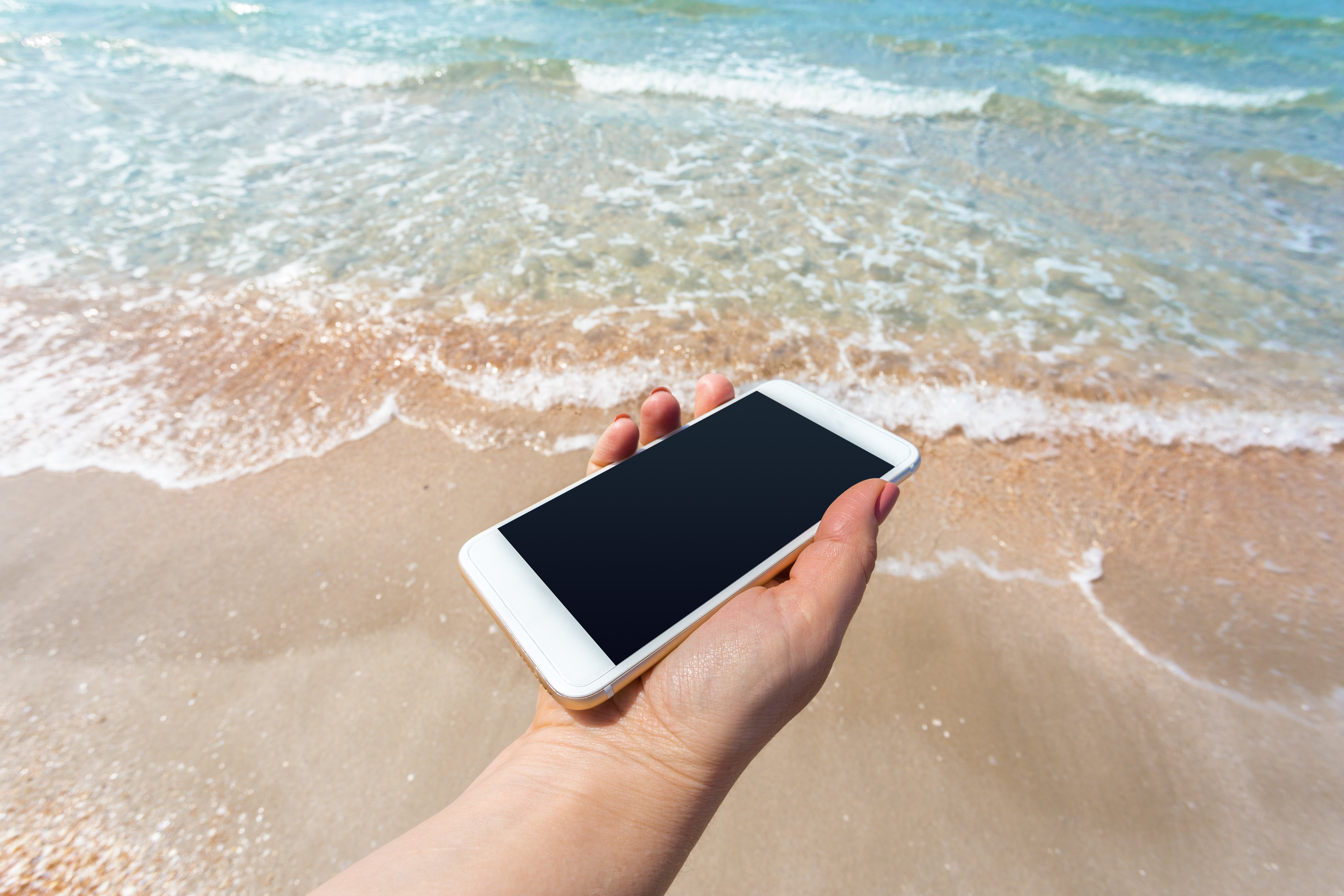 beautiful-womans-hand-using-smart-phone-beach