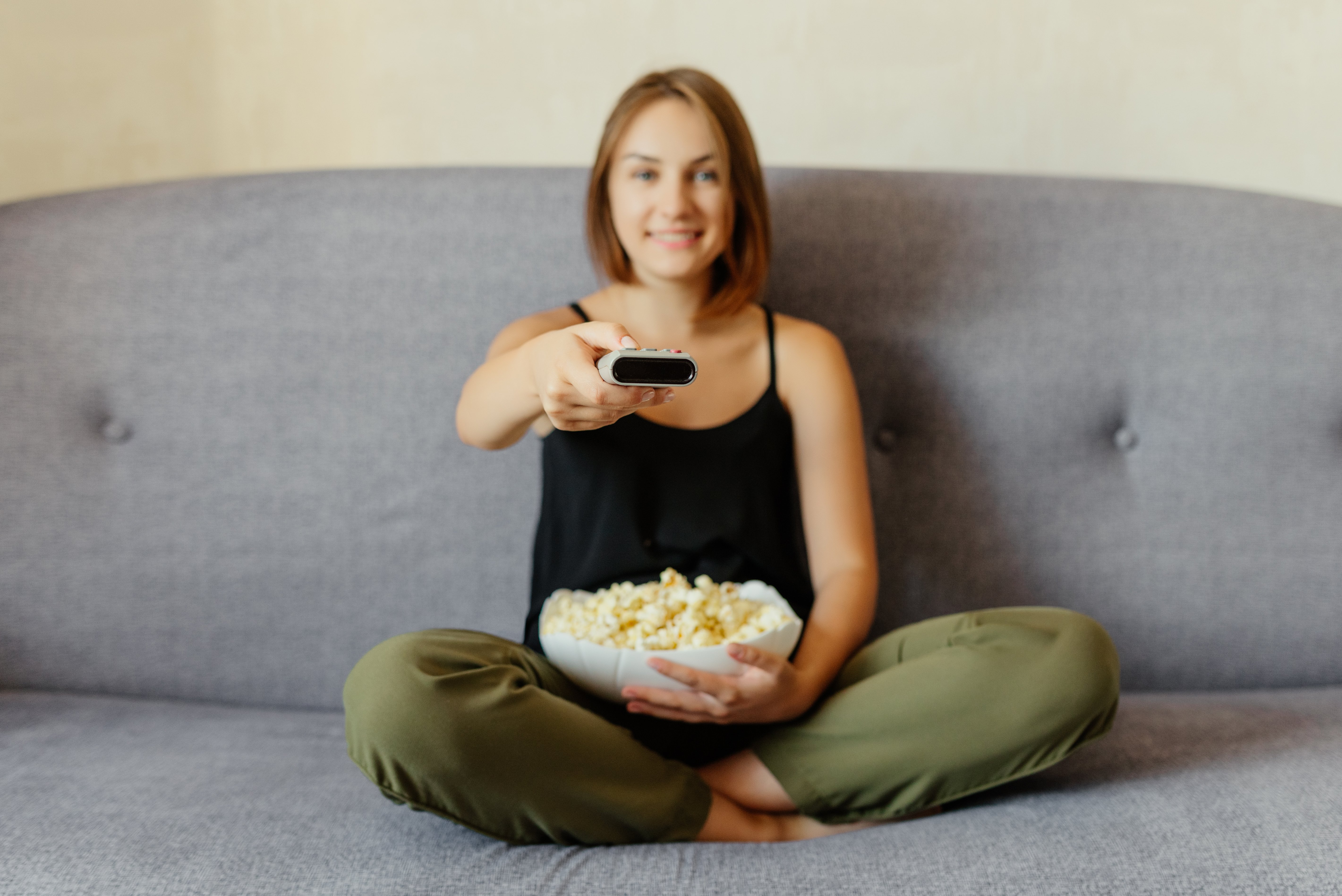 cheerful-attractive-girl-with-popcorn-sitting-sofa-watching-tv-changing-channels-with-remote-control-eating-popcorn-home