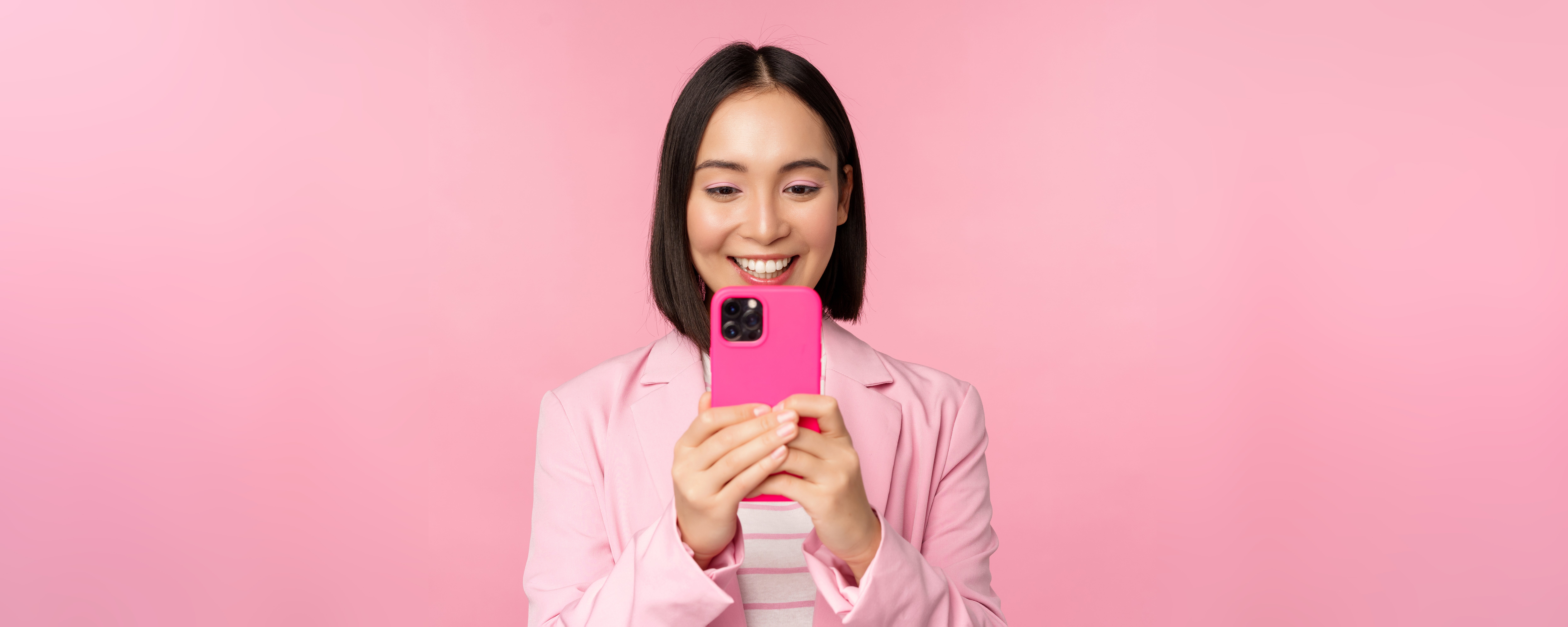 image-of-smiling-asian-corporate-woman-in-suit-looking-watching-on-smartphone-app-using-mobile-phone